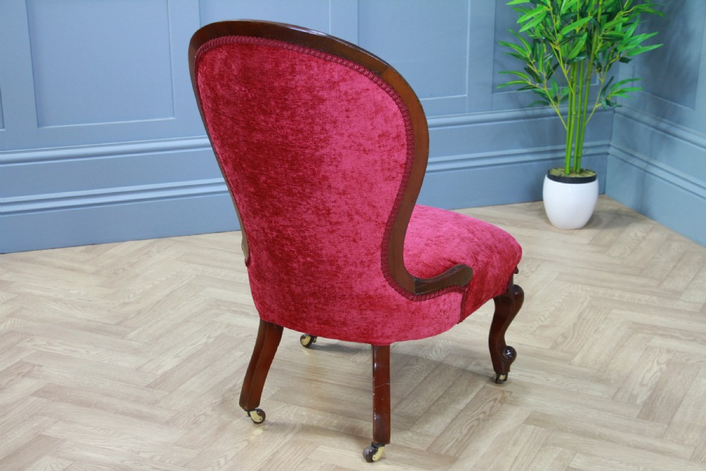 An antique Victorian balloon back nursing chair with a carved mahogany frame and deep pink velvet upholstery resting on castors. View XI