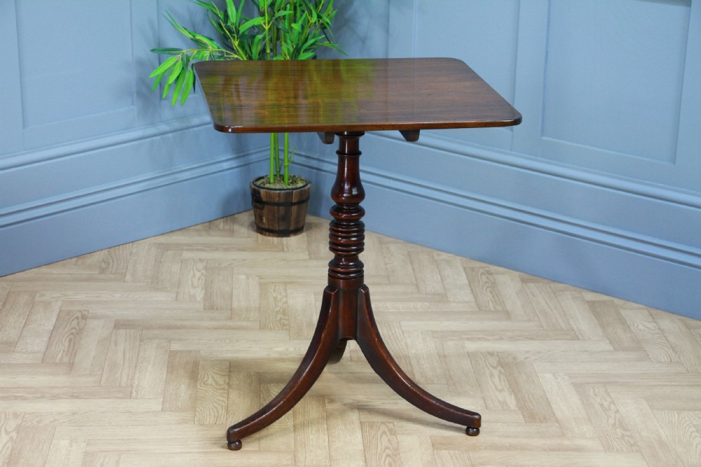 A Regency mahogany tilt-top wine table with a rounded square top, a turned column, and three splayed legs.