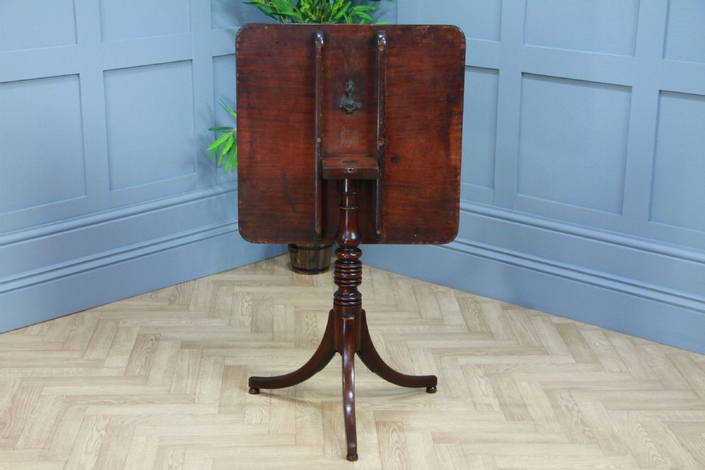 A Regency mahogany tilt-top wine table with a rounded square top, a turned column, and three splayed legs. View V