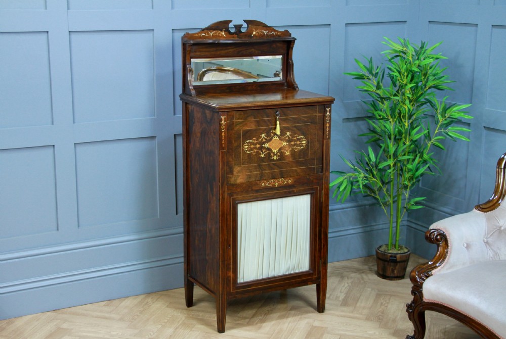 An Edwardian rosewood ladies bureau cabinet featuring marquetry inlay, a mirrored superstructure, a fall-front desk section, and a lower cupboard with a pleated fabric panel.