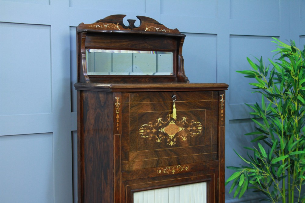 An Edwardian rosewood ladies bureau cabinet featuring marquetry inlay, a mirrored superstructure, a fall-front desk section, and a lower cupboard with a pleated fabric panel. View VI
