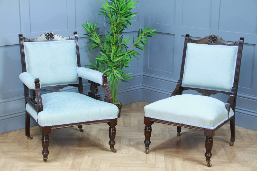 Pair of Edwardian mahogany armchairs upholstered in pale blue fabric featuring carved crestings and turned legs with brass castors.
