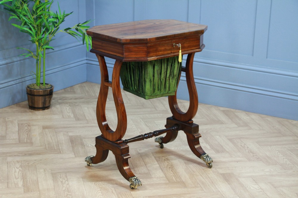 An antique Regency kingwood work table featuring lyre-shaped side supports, a suspended green pleated fabric box, and brass paw feet on castors.