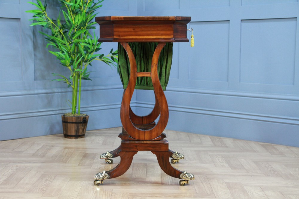 An antique Regency kingwood work table featuring lyre-shaped side supports, a suspended green pleated fabric box, and brass paw feet on castors. View IX