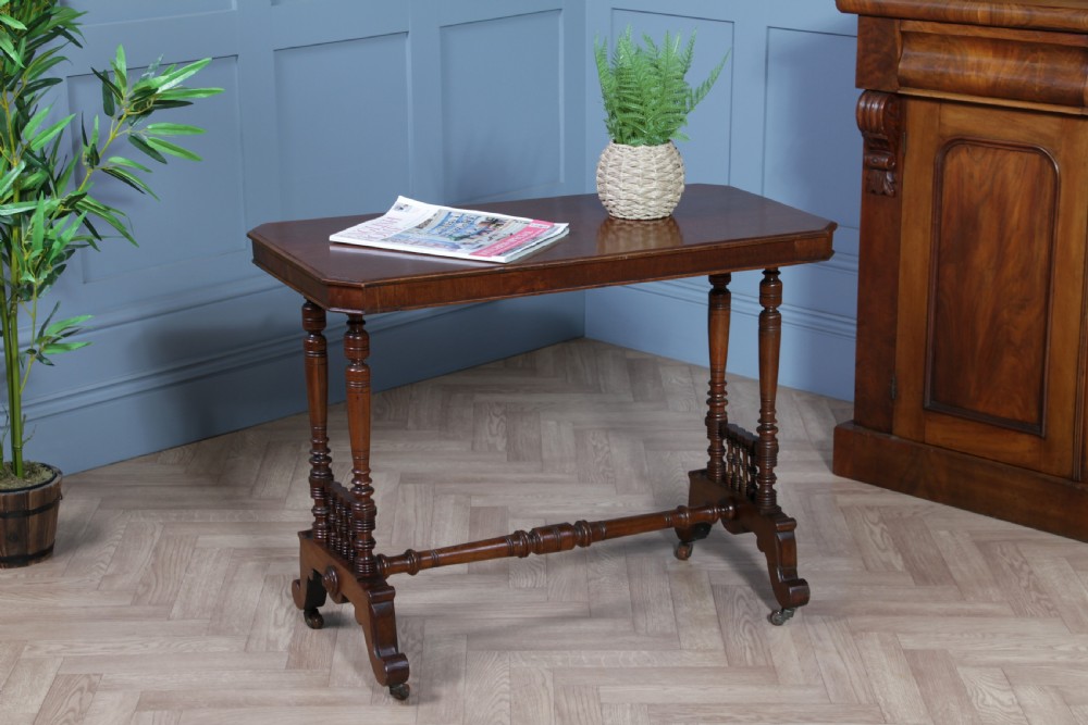 A late Victorian turned walnut occasional table featuring a rectangular top, twin turned end supports, a low stretcher, and feet set on castors.