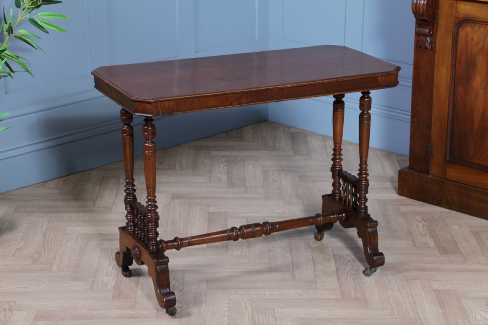 A late Victorian turned walnut occasional table featuring a rectangular top, twin turned end supports, a low stretcher, and feet set on castors. View II