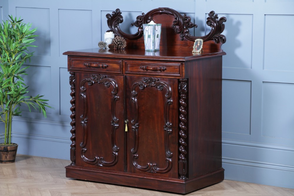 A 19th-century dark mahogany chiffonier featuring two top drawers, two carved panel cupboard doors, barley twist side columns, and a carved scroll splashback.