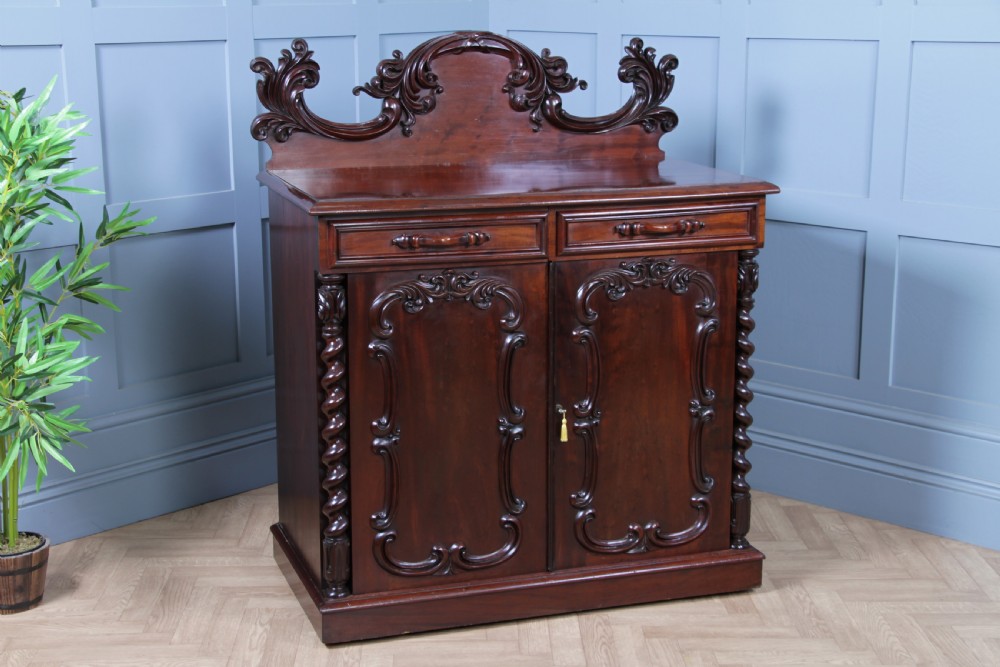 A 19th-century dark mahogany chiffonier featuring two top drawers, two carved panel cupboard doors, barley twist side columns, and a carved scroll splashback. View II