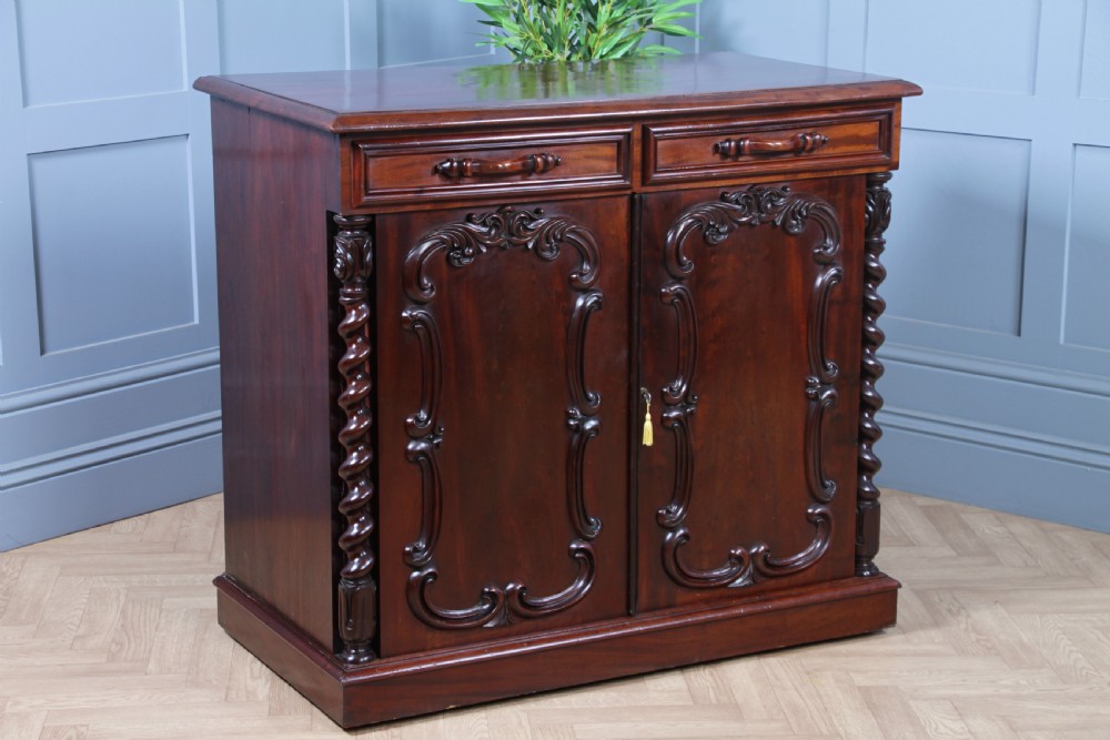 A 19th-century dark mahogany chiffonier featuring two top drawers, two carved panel cupboard doors, barley twist side columns, and a carved scroll splashback. View V