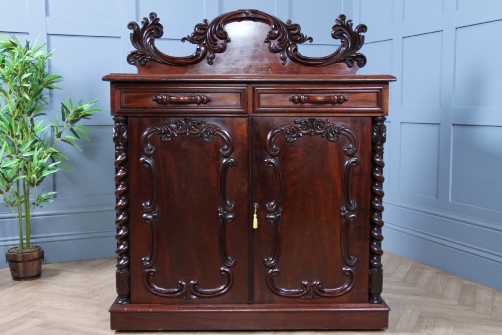 A 19th-century dark mahogany chiffonier featuring two top drawers, two carved panel cupboard doors, barley twist side columns, and a carved scroll splashback. View VI