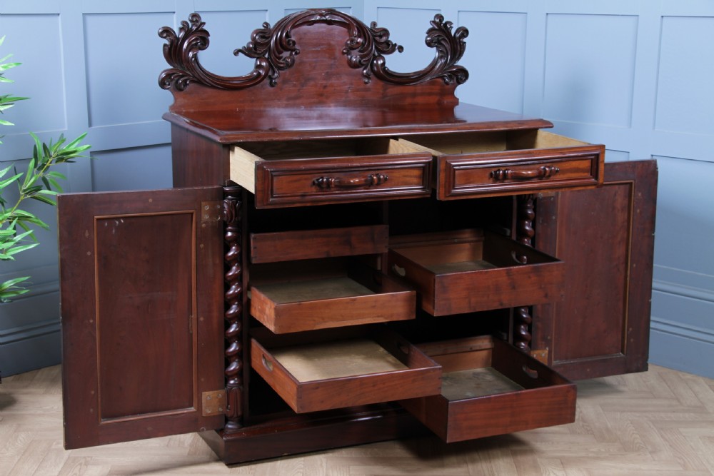 A 19th-century dark mahogany chiffonier featuring two top drawers, two carved panel cupboard doors, barley twist side columns, and a carved scroll splashback. View XV