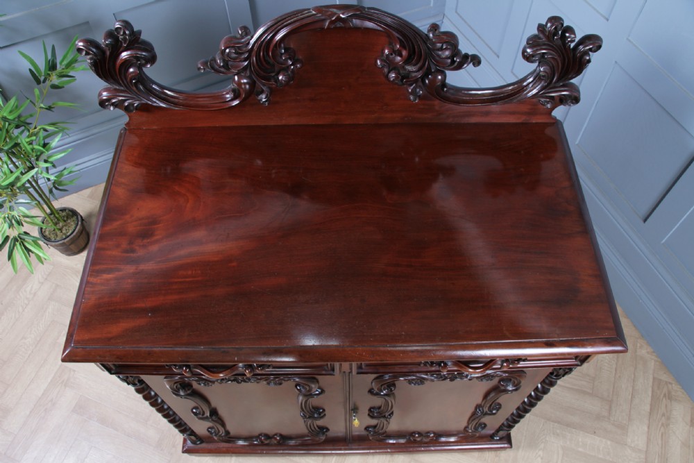 A 19th-century dark mahogany chiffonier featuring two top drawers, two carved panel cupboard doors, barley twist side columns, and a carved scroll splashback. View XVI
