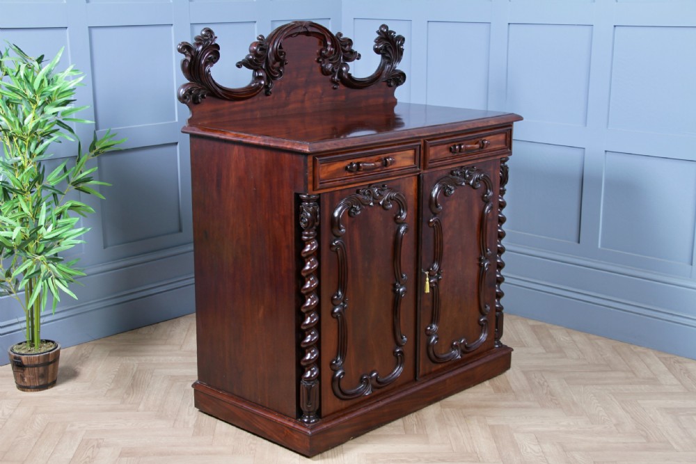 A 19th-century dark mahogany chiffonier featuring two top drawers, two carved panel cupboard doors, barley twist side columns, and a carved scroll splashback. View XVII