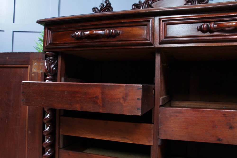 A 19th-century dark mahogany chiffonier featuring two top drawers, two carved panel cupboard doors, barley twist side columns, and a carved scroll splashback. View XVIII