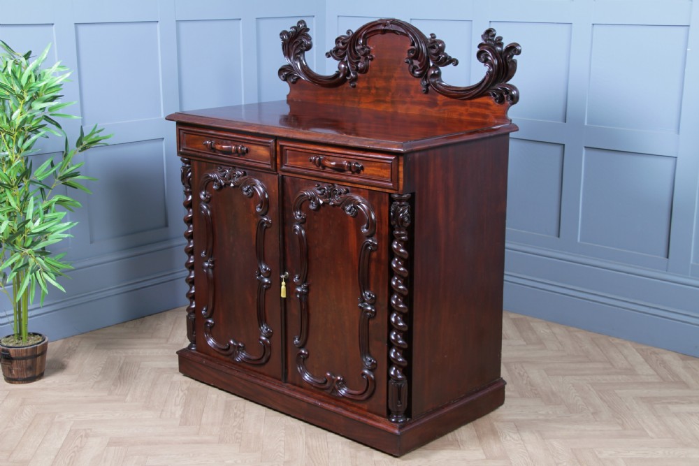 A 19th-century dark mahogany chiffonier featuring two top drawers, two carved panel cupboard doors, barley twist side columns, and a carved scroll splashback. View XXI