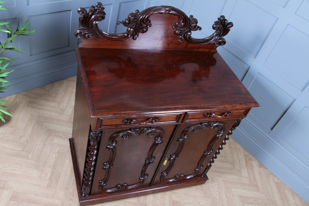 A 19th-century dark mahogany chiffonier featuring two top drawers, two carved panel cupboard doors, barley twist side columns, and a carved scroll splashback. View XXIII