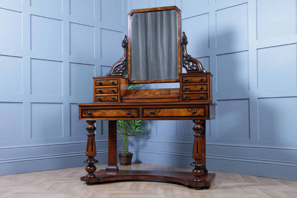 An antique Victorian burr walnut duchess dressing table featuring an integrated swing mirror, jewellery drawers, a curved piano top lid, turned front legs, and a plinth base. View II