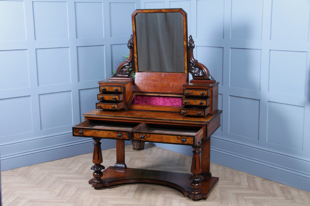 An antique Victorian burr walnut duchess dressing table featuring an integrated swing mirror, jewellery drawers, a curved piano top lid, turned front legs, and a plinth base. View III