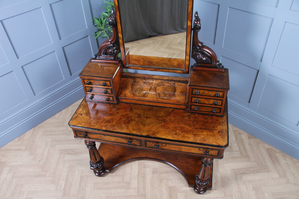 An antique Victorian burr walnut duchess dressing table featuring an integrated swing mirror, jewellery drawers, a curved piano top lid, turned front legs, and a plinth base. View VI
