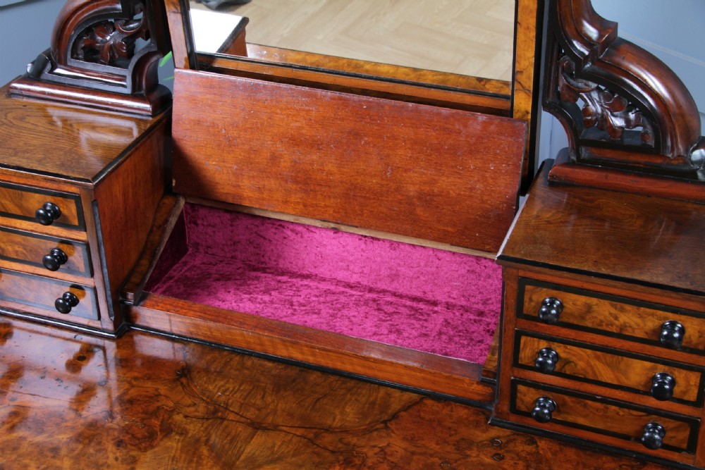 An antique Victorian burr walnut duchess dressing table featuring an integrated swing mirror, jewellery drawers, a curved piano top lid, turned front legs, and a plinth base. View VII