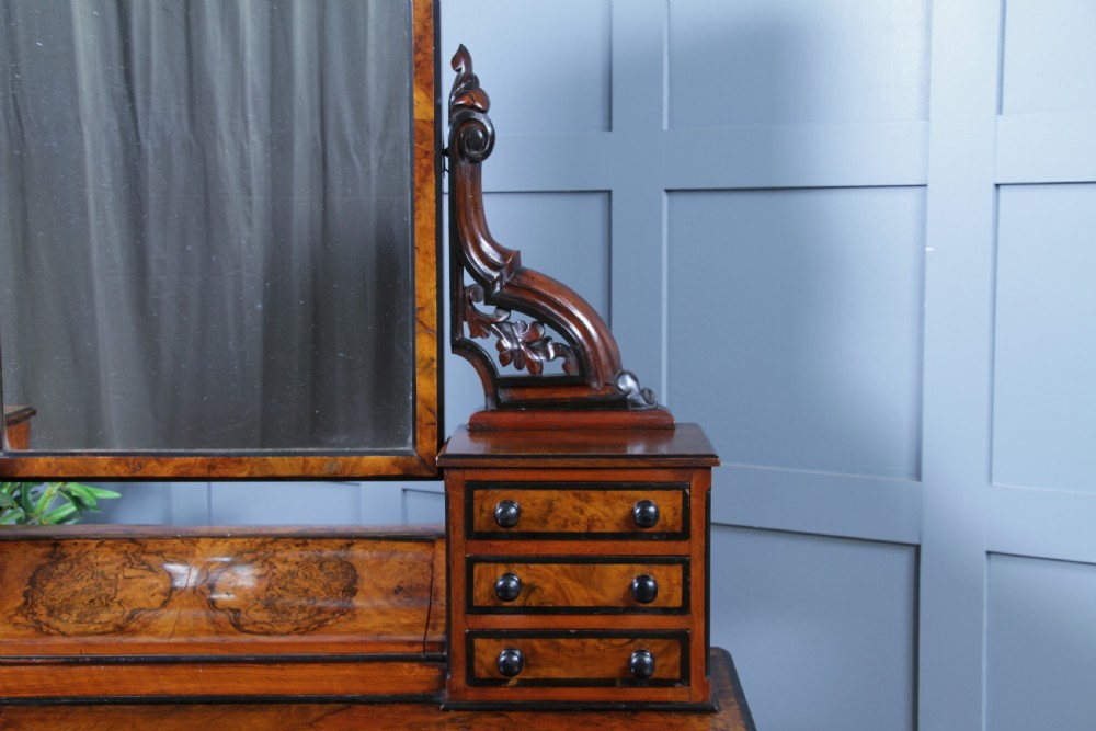 An antique Victorian burr walnut duchess dressing table featuring an integrated swing mirror, jewellery drawers, a curved piano top lid, turned front legs, and a plinth base. View IX