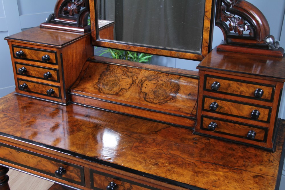 An antique Victorian burr walnut duchess dressing table featuring an integrated swing mirror, jewellery drawers, a curved piano top lid, turned front legs, and a plinth base. View X