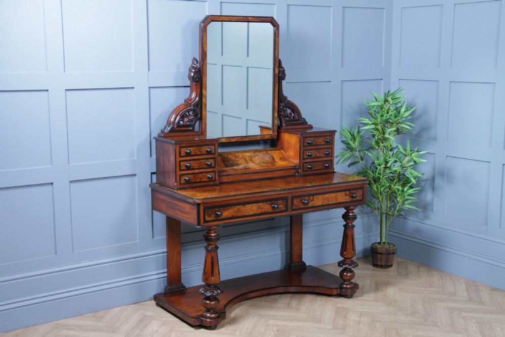 An antique Victorian burr walnut duchess dressing table featuring an integrated swing mirror, jewellery drawers, a curved piano top lid, turned front legs, and a plinth base. View XI