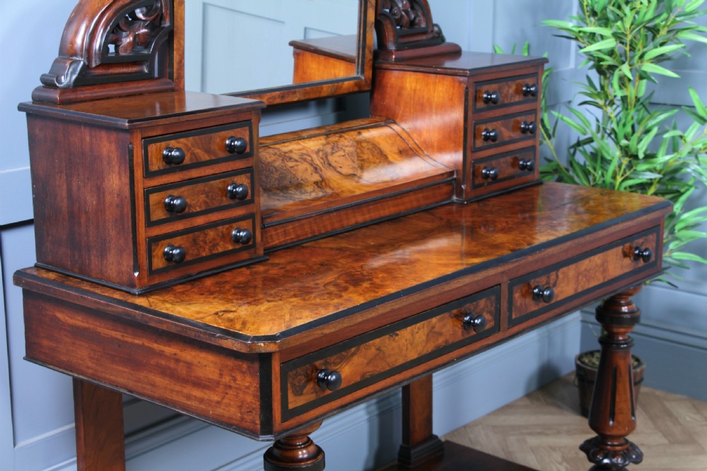 An antique Victorian burr walnut duchess dressing table featuring an integrated swing mirror, jewellery drawers, a curved piano top lid, turned front legs, and a plinth base. View XIII