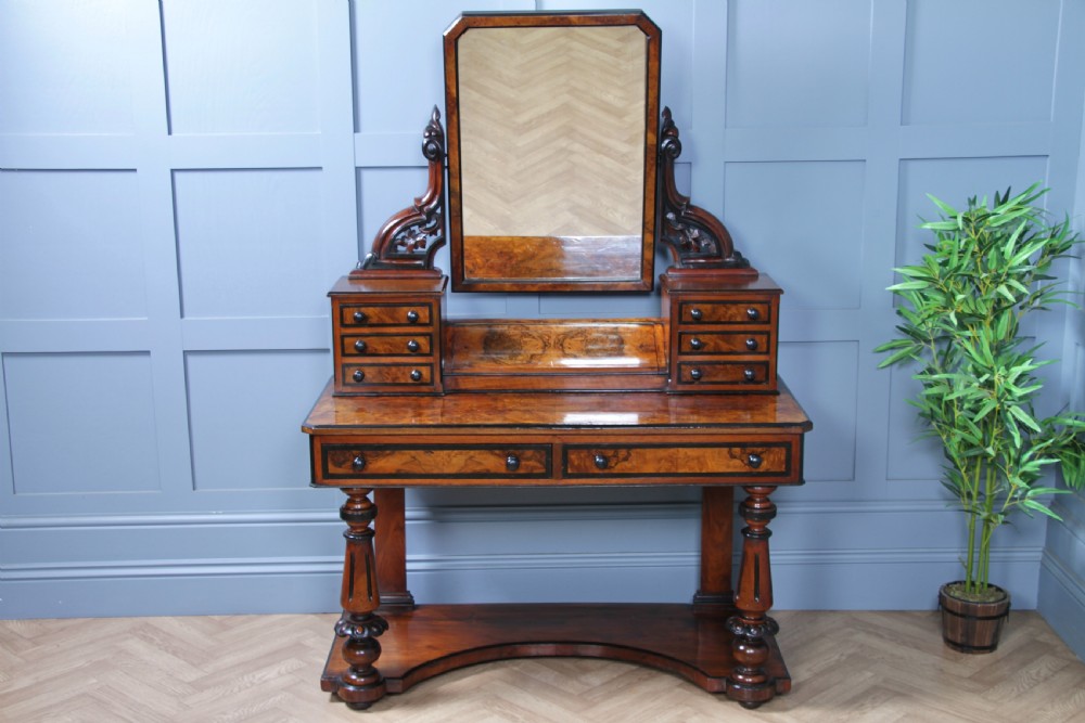 An antique Victorian burr walnut duchess dressing table featuring an integrated swing mirror, jewellery drawers, a curved piano top lid, turned front legs, and a plinth base. View XIV
