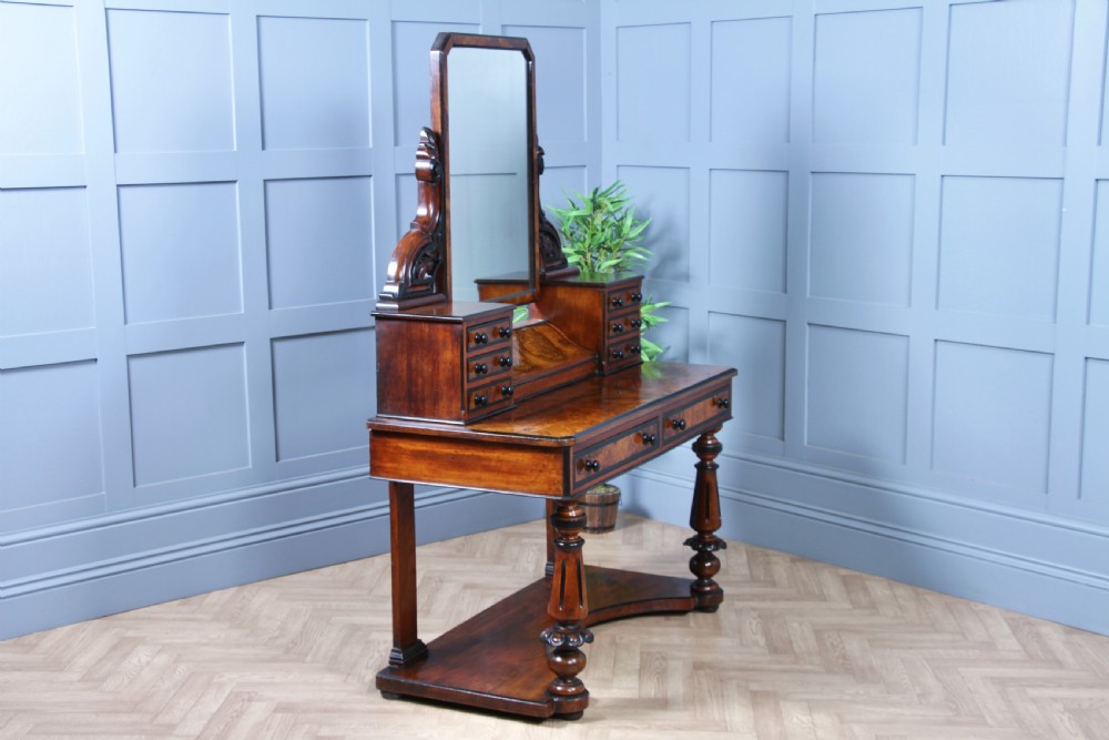 An antique Victorian burr walnut duchess dressing table featuring an integrated swing mirror, jewellery drawers, a curved piano top lid, turned front legs, and a plinth base. View XV