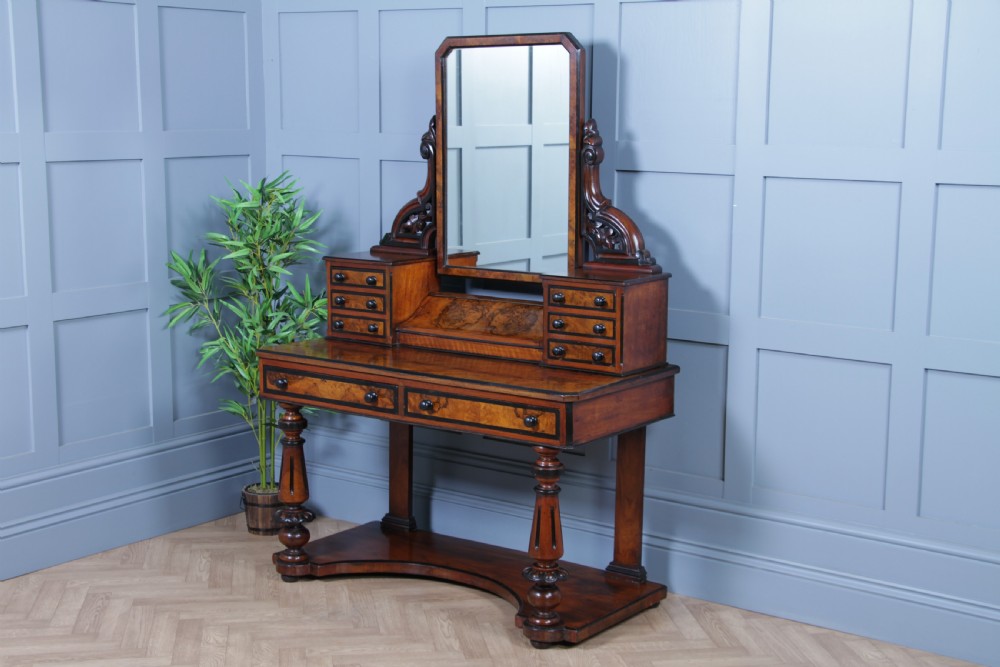 An antique Victorian burr walnut duchess dressing table featuring an integrated swing mirror, jewellery drawers, a curved piano top lid, turned front legs, and a plinth base. View XVII