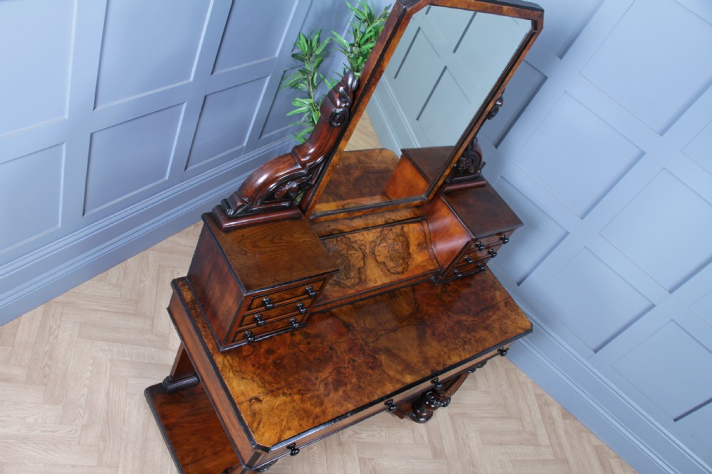 An antique Victorian burr walnut duchess dressing table featuring an integrated swing mirror, jewellery drawers, a curved piano top lid, turned front legs, and a plinth base. View XXV