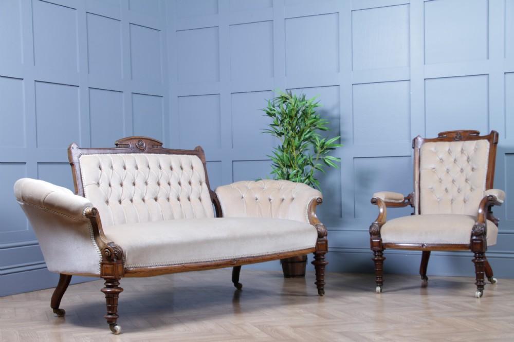 A Victorian carved walnut two-piece salon suite comprising a button-tufted cream velvet sofa and a matching armchair on turned legs with castors.
