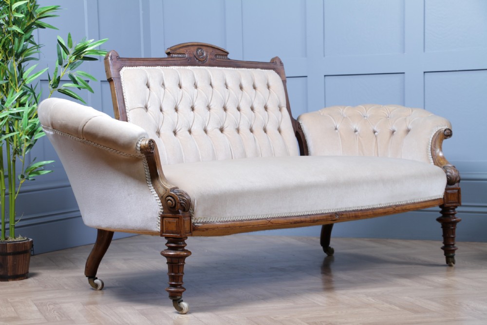 A Victorian carved walnut two-piece salon suite comprising a button-tufted cream velvet sofa and a matching armchair on turned legs with castors. View II