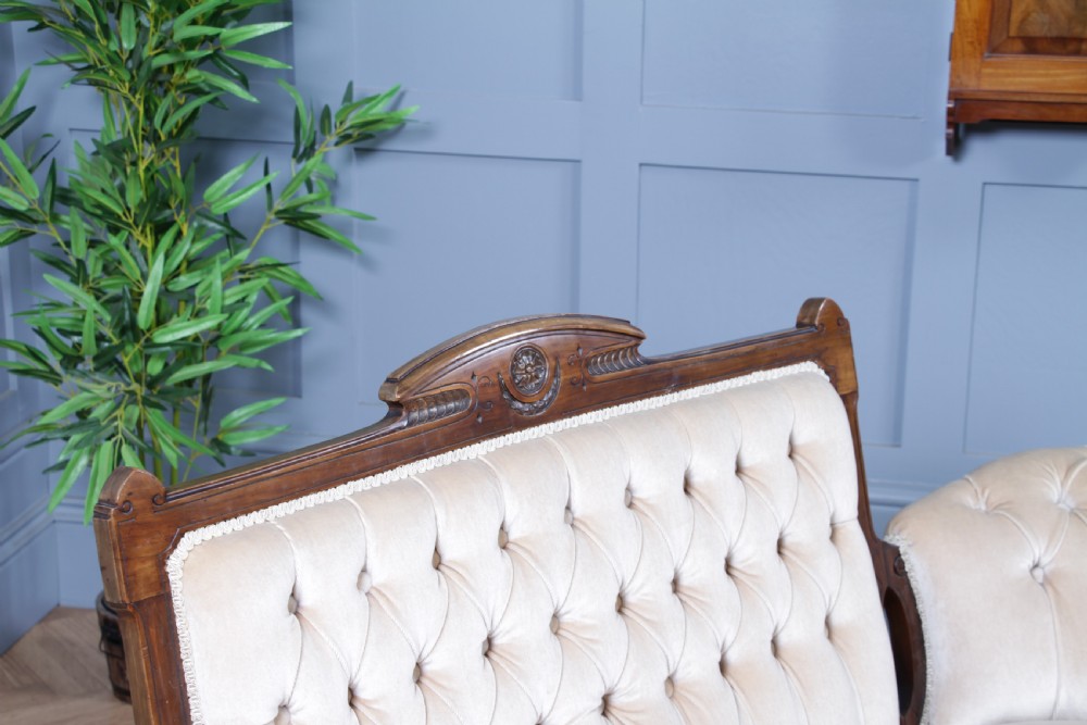 A Victorian carved walnut two-piece salon suite comprising a button-tufted cream velvet sofa and a matching armchair on turned legs with castors. View VII