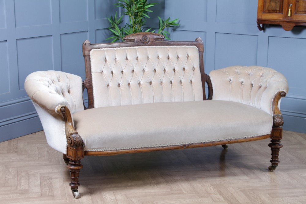 A Victorian carved walnut two-piece salon suite comprising a button-tufted cream velvet sofa and a matching armchair on turned legs with castors. View VIII