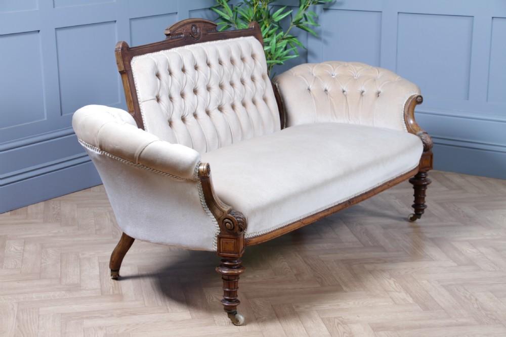A Victorian carved walnut two-piece salon suite comprising a button-tufted cream velvet sofa and a matching armchair on turned legs with castors. View IX