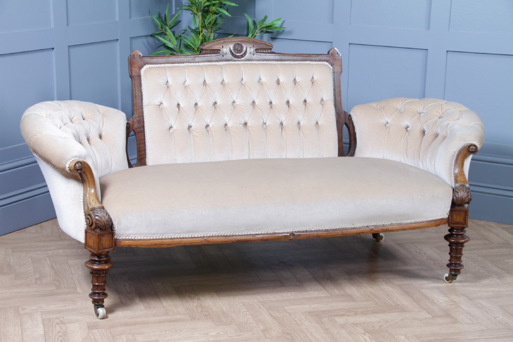 A Victorian carved walnut two-piece salon suite comprising a button-tufted cream velvet sofa and a matching armchair on turned legs with castors. View X