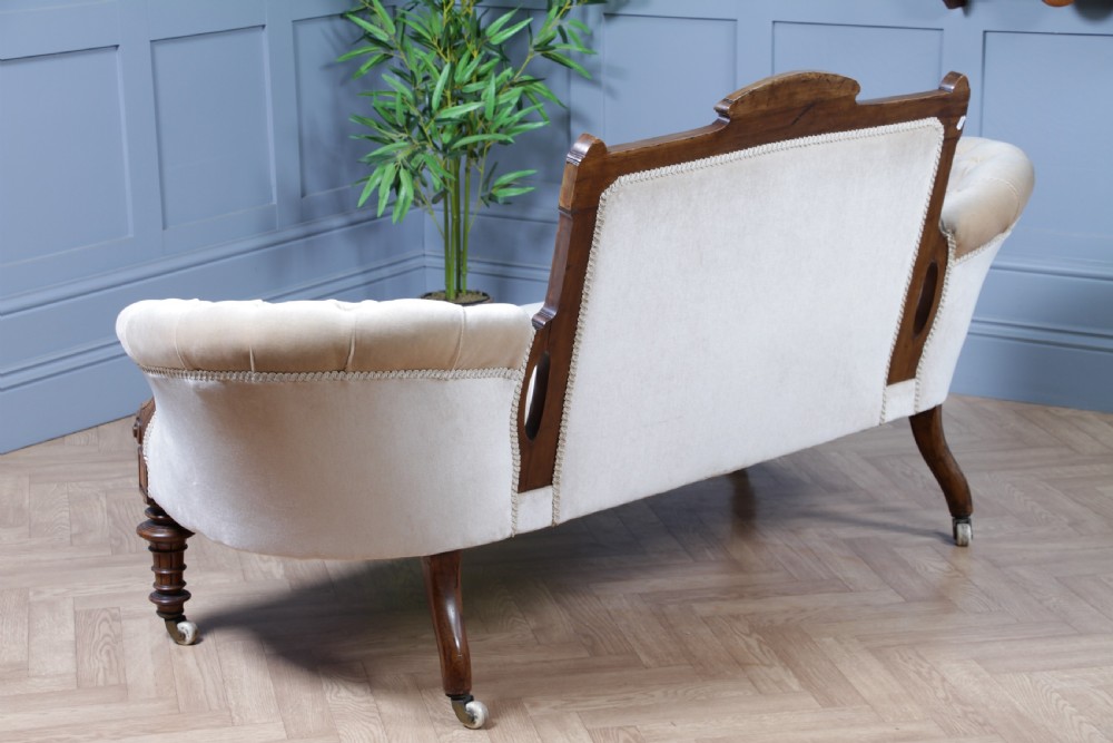 A Victorian carved walnut two-piece salon suite comprising a button-tufted cream velvet sofa and a matching armchair on turned legs with castors. View XI