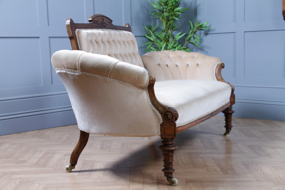 A Victorian carved walnut two-piece salon suite comprising a button-tufted cream velvet sofa and a matching armchair on turned legs with castors. View XIV