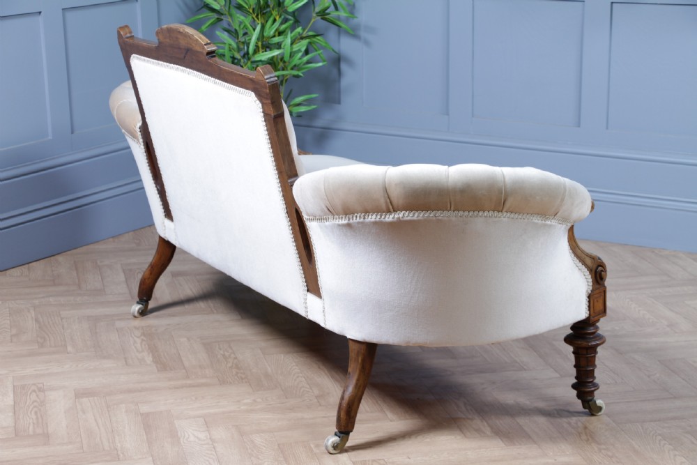 A Victorian carved walnut two-piece salon suite comprising a button-tufted cream velvet sofa and a matching armchair on turned legs with castors. View XV