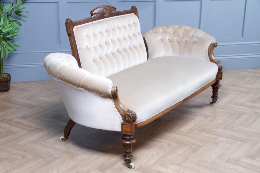 A Victorian carved walnut two-piece salon suite comprising a button-tufted cream velvet sofa and a matching armchair on turned legs with castors. View XX