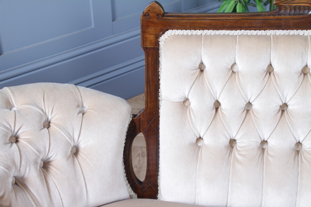 A Victorian carved walnut two-piece salon suite comprising a button-tufted cream velvet sofa and a matching armchair on turned legs with castors. View XXI
