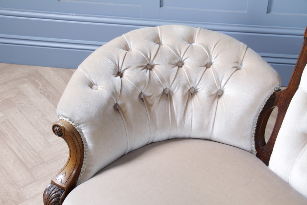 A Victorian carved walnut two-piece salon suite comprising a button-tufted cream velvet sofa and a matching armchair on turned legs with castors. View XXII