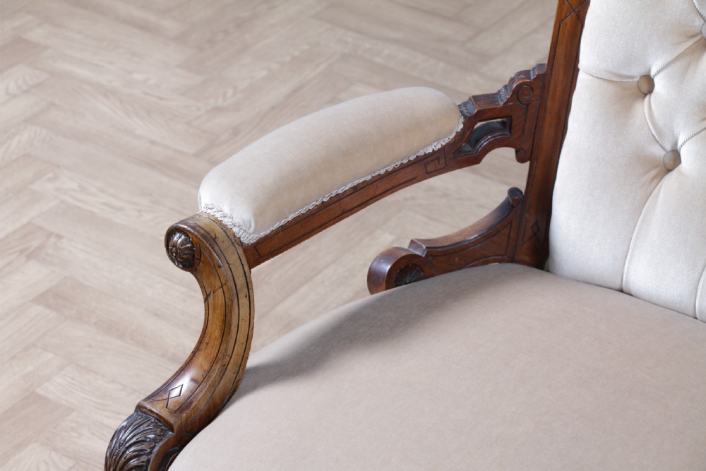 A Victorian carved walnut two-piece salon suite comprising a button-tufted cream velvet sofa and a matching armchair on turned legs with castors. View XXVI