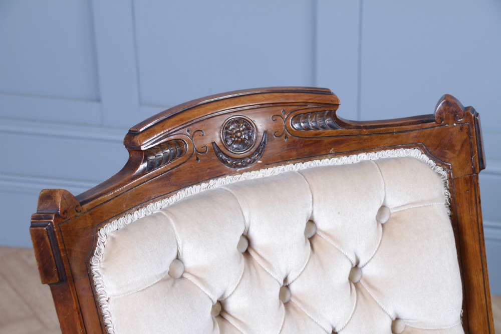 A Victorian carved walnut two-piece salon suite comprising a button-tufted cream velvet sofa and a matching armchair on turned legs with castors. View XXVII