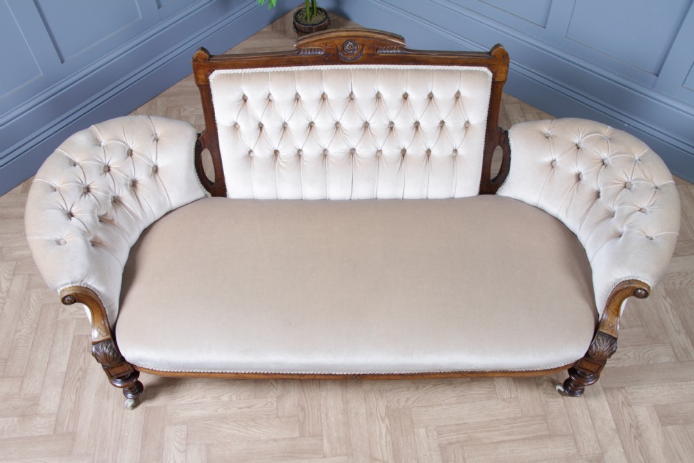 A Victorian carved walnut two-piece salon suite comprising a button-tufted cream velvet sofa and a matching armchair on turned legs with castors. View VI