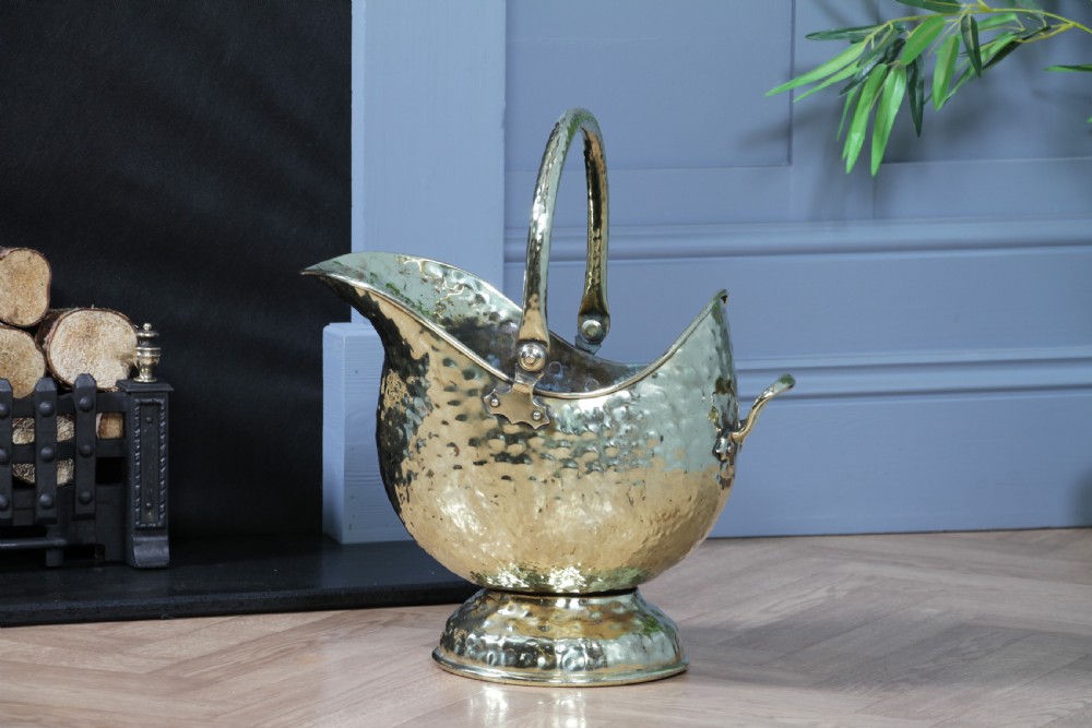 A Victorian hand-hammered brass helmet-shaped coal scuttle featuring a top swing handle, rear loop handle, and a round pedestal base. View III