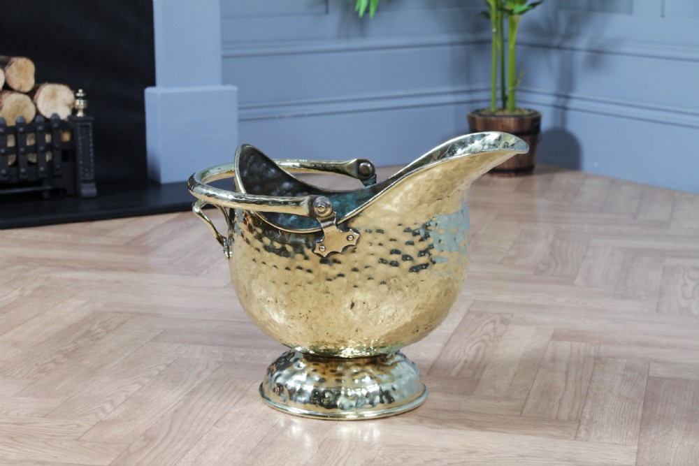 A Victorian hand-hammered brass helmet-shaped coal scuttle featuring a top swing handle, rear loop handle, and a round pedestal base. View XIII