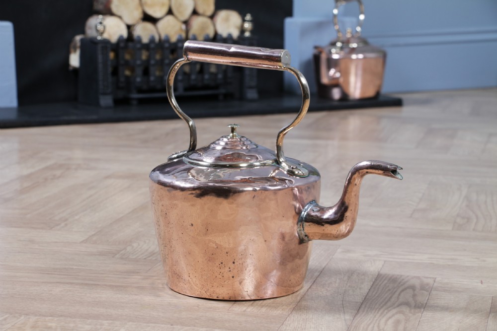 A polished George III copper kettle with a raised brass fixed handle and a curved gooseneck spout.